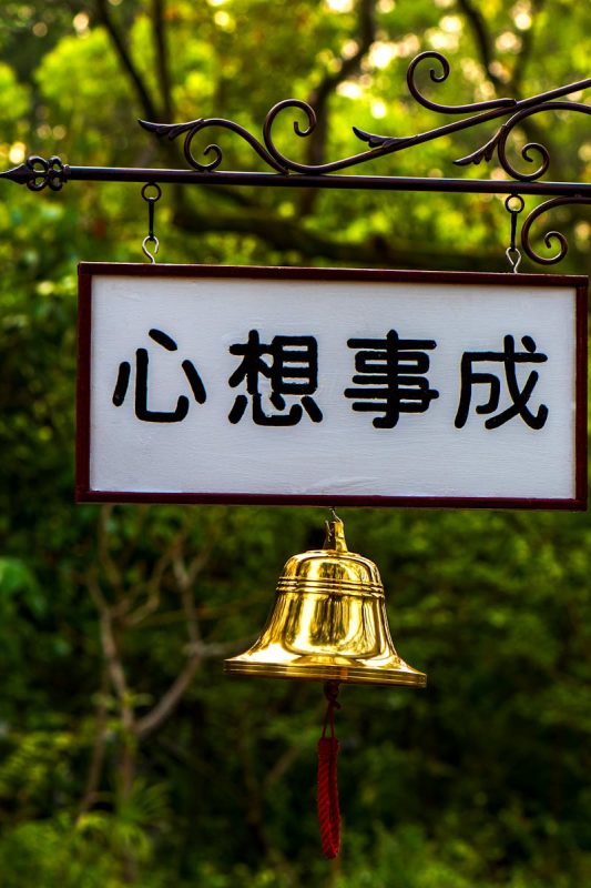 Outdoor signage with a golden bell in a lush Taipei park setting, conveying tranquility.