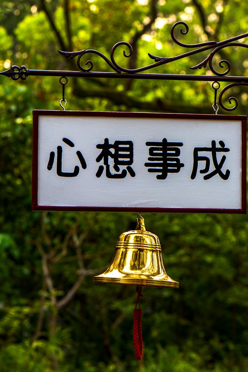 Outdoor signage with a golden bell in a lush Taipei park setting, conveying tranquility.